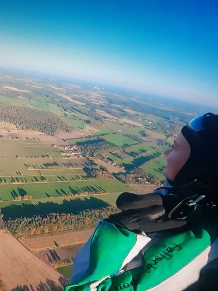 Die Bloggerin Juliane und ihr Tandemmaster Ralf über grünen Wiesen und Wäldern, goldenen Feldern und das Meer am Horizont. Dort oben sieht man, dass die Erde eine Kugel ist.