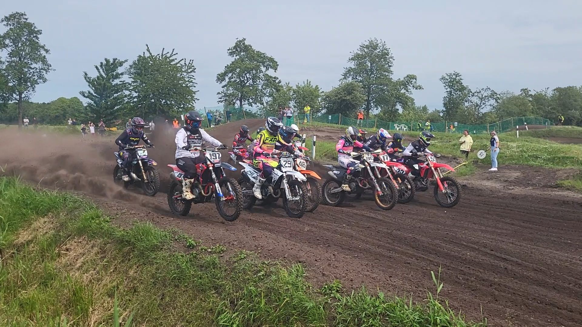 Viele bunte Motorräder mit bunt eingekleideten Fahr:innen wirbeln direkt nach dem Start eine Menge Staub auf.
