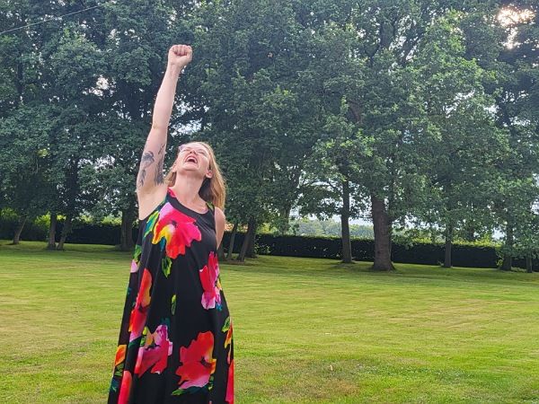 Bloggerin Juliane Kau steht im grünen Garten. Sie reckt die Faust in die Luft und freut sich über ihren Erfolg. 