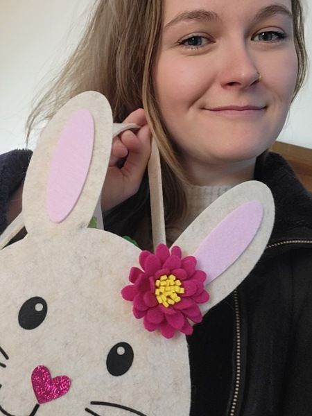 Bloggerin Juliane Kau hält lächelnd ein süßes Osterkörbchen in der Hand, dass aussieht wie ein hasen-Mädchen mit dunkel roter Blume am Ohr und einer glitzernden herzförmigen Nase